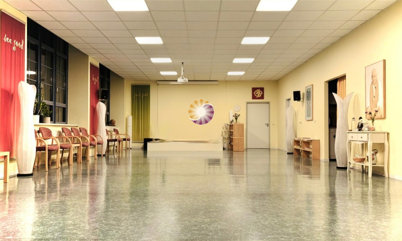 Großer, heller Übungsraum des Qi Gong Vital Zentrums in Radebeul mit Stuhlreihe, roten Wandbehängen und dem Logo an der Stirnwand