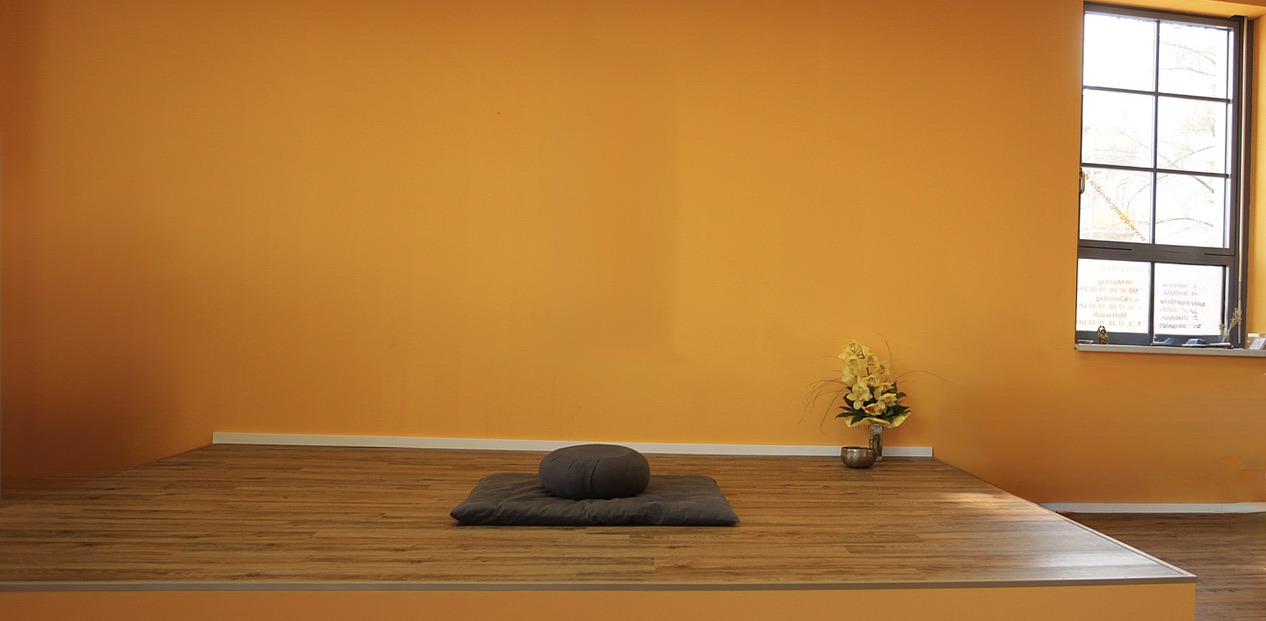 Ruhiger Meditationsplatz: Sitzkissen auf einer Matte auf dem Holzpodest vor der orangefarbenen Wand